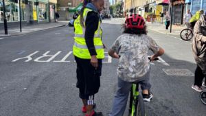 Child being assisted to ride a bike at London Cycle Festival - Sunday Streets at Church Street as part of World Car Free Day